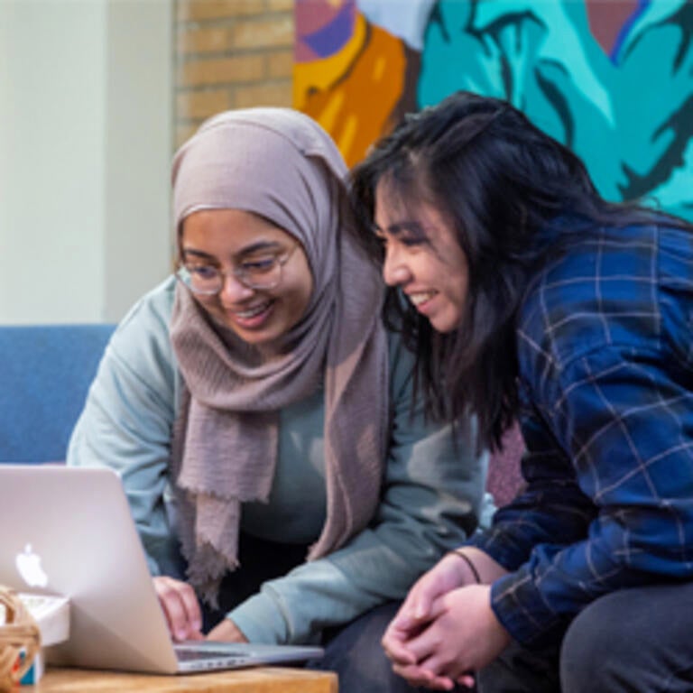 Two students smile while looking over a shared laptop within the Asian Pacific student center