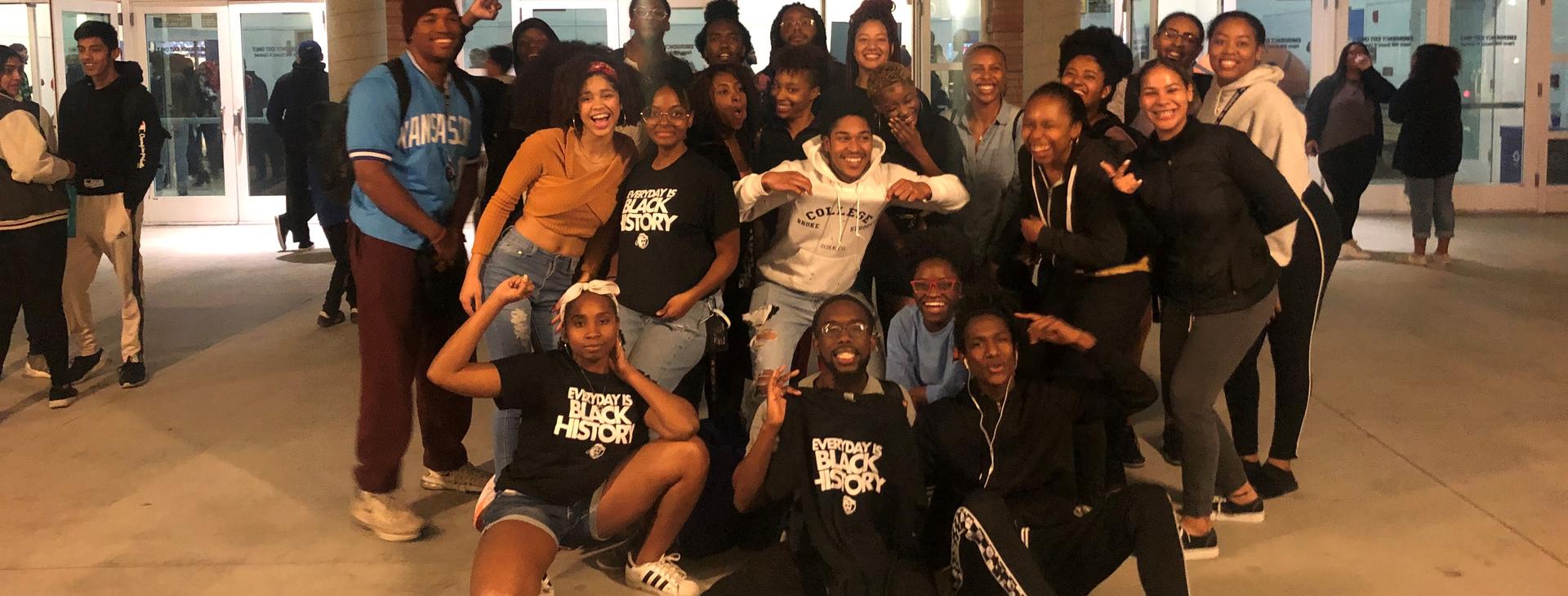 A large group of students gather for a group photo outside the Student Recreation Center at UCR