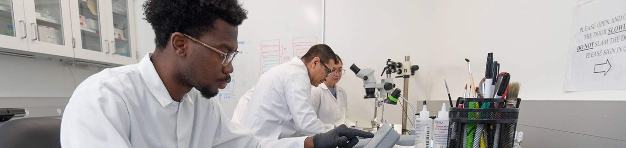 Researcher working on machine, with two other researchers in the background