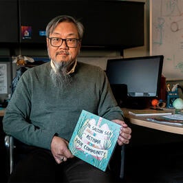 David Lo sitting at desk holding comic book. by Kitra Cahana for Undark