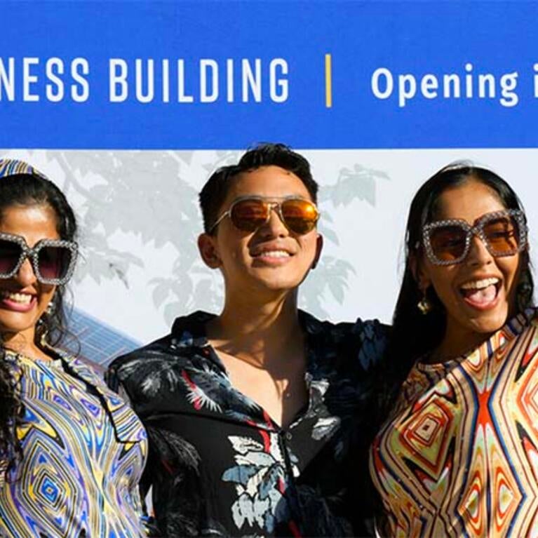 Fall Welcome 2023 party, 3 students in front of New Business Building backdrop