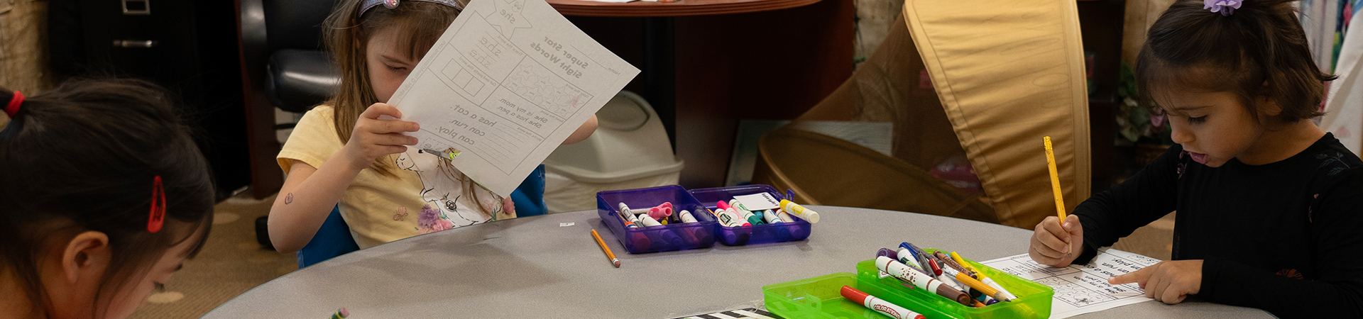 child cutting paper and child writing at table