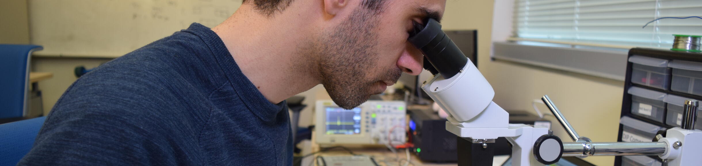 Man looking through a microscope while using tweezers.