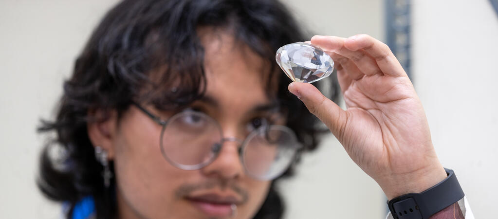 Student closely examines a faceted crystal gem to study light scattering effects, specifically Mie scattering phenomena.