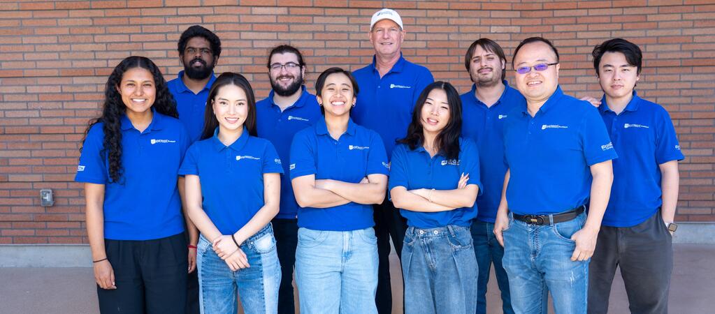 The UCR EcoCAR team poses in front of a brick wall, wearing matching blue team shirts, at the Year 3 Winter Workshop hosted by CARB at the UCR School of Business