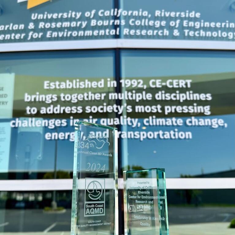 A glass award displayed in front of the University of California, Riverside's CE-CERT building, reflecting the text "University of California, Riverside Bourns College of Engineering Center for Environmental Research & Technology." The award is from the South Coast Air Quality Management District, recognizing the center for "Leadership in Air Quality." The background text highlights CE-CERT's mission to address air quality, climate change, energy, and transportation challenges