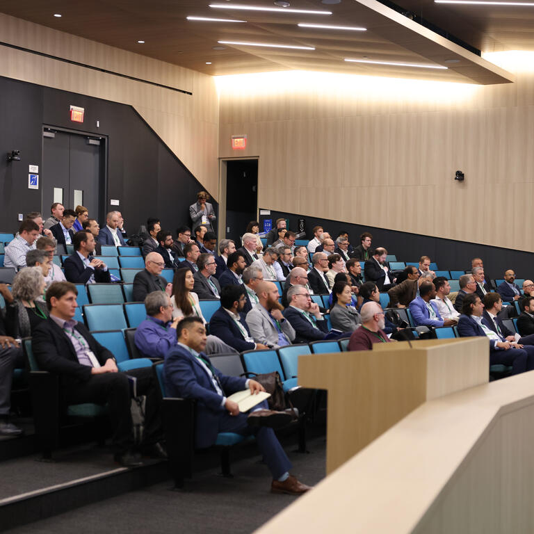 Audience members listen to a presentation in a large lecture hall during the Inaugural Hydrogen Engine Alliance – North America Conference, with keynote speaker Professor Thomas Koch presenting at the front.