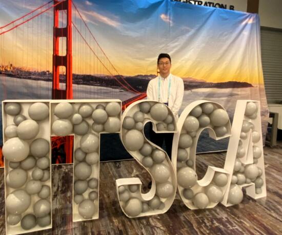 Dongbo Peng, CE-CERT graduate student, stands in front of large ITSCA letters surrounded by a silver balloon display, with an image of the Golden Gate Bridge in the background, at the ITSCA 2024 conference.