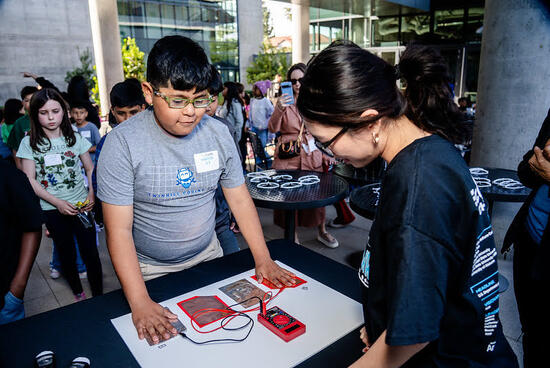 A young student interacts with a hands-on STEM activity, testing electrical circuits with guidance from a UCR EcoCAR team member during a community outreach event.