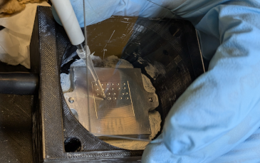 Close-up of a pipette depositing liquid onto a cold stage with a metal grid, used in atmospheric research at UCR CE-CERT.