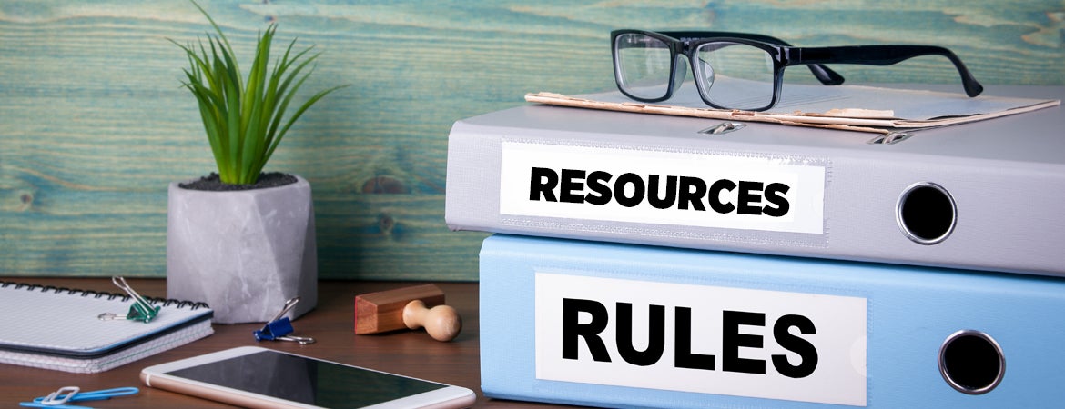 Binders containing resources and rules are stacked up on a desk. 