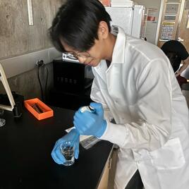 male student working in a lab wearing a white lab coat 