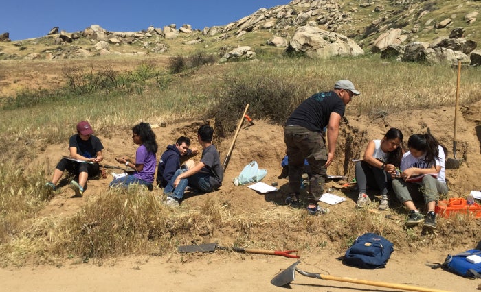 Group of undergraduate students collecting soil samples with shovels at mountains.