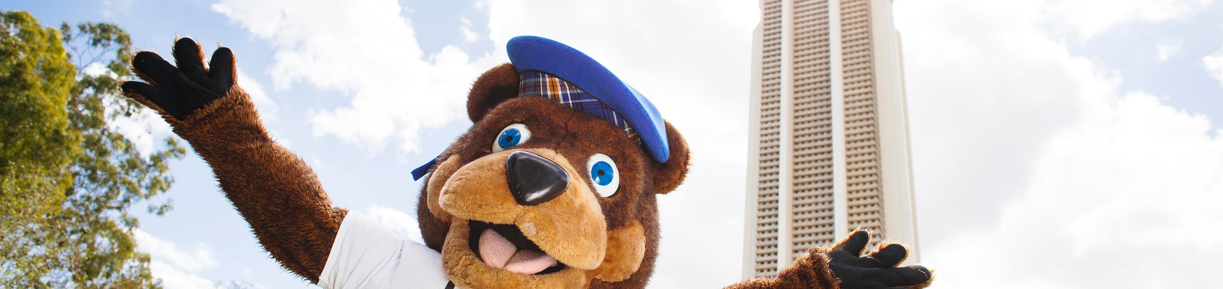 UCR Scotty Bear mascot wearing I Love UCR tshirt with arms raised in front of belltower on UCR campus.