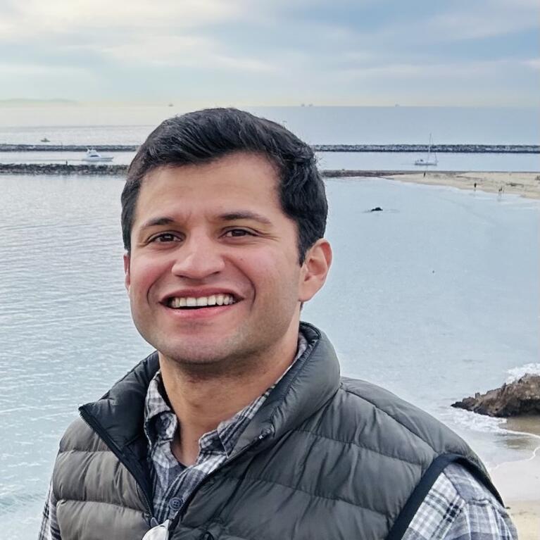 Chris in a puffer vest standing in front of body of water, smiling. 