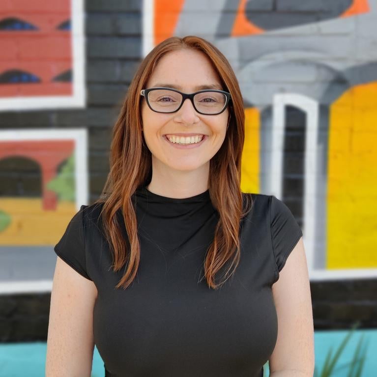 Kyla in a black dress, seen from the waist up, smiling at the camera in front of a colorful backdrop
