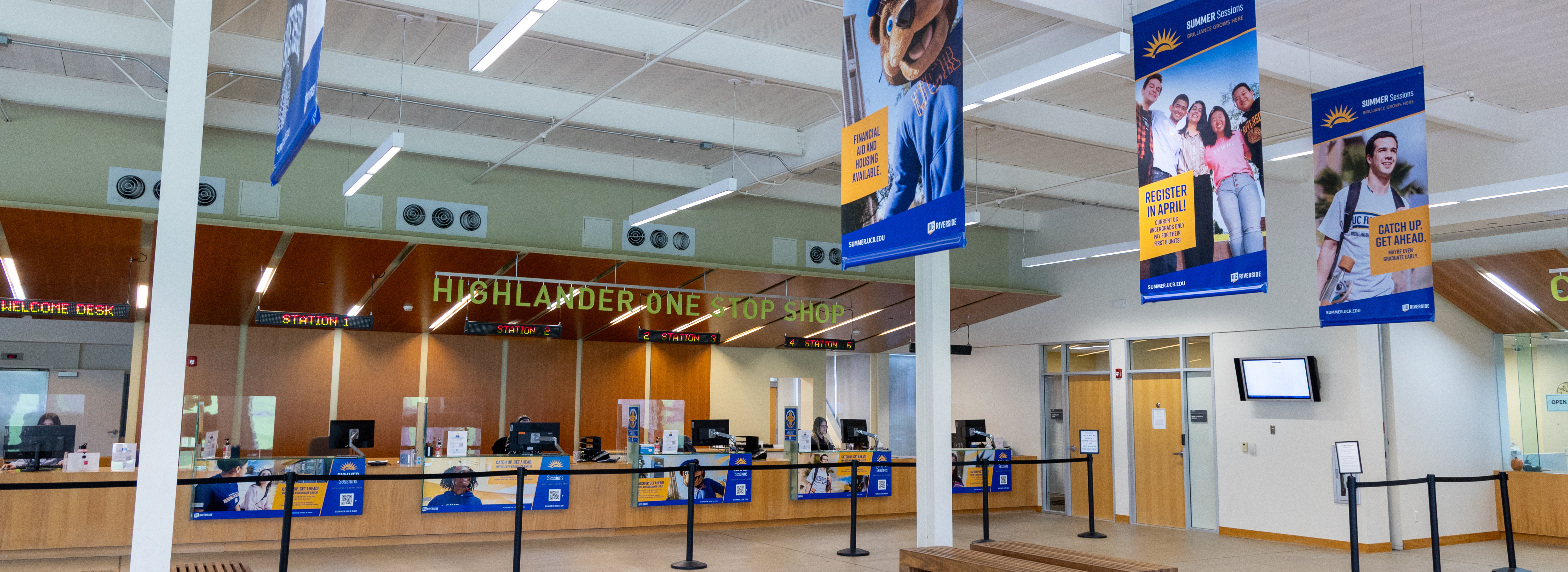 A wide image of the HOSS lobby including UCR banners hanging and a large sign over help desks that reads "Highlander One-Stop Shop"