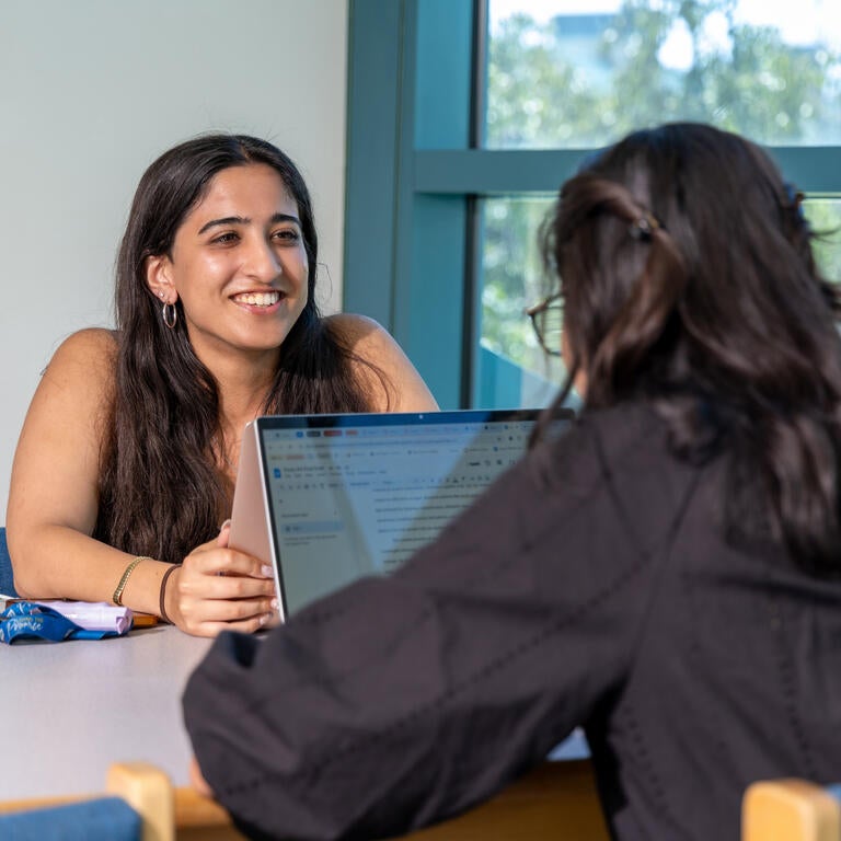 Two students talk to each other at a table