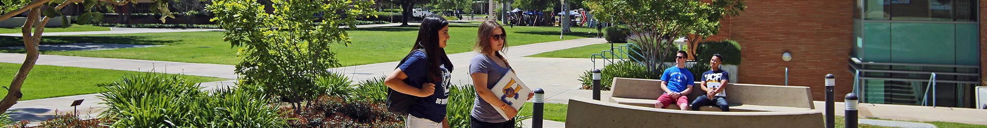 Panoramic view of UCR's parklike campus with students sitting on a bench and walking to class.