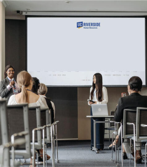 African American woman giving a presentation to a live audience at a Benefits Workshop 