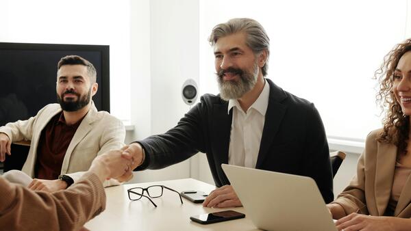 Four professional individuals sitting at a table with two of them shaking hands to show management