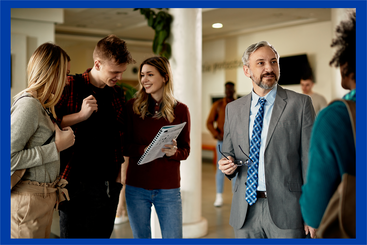 Group of 3 people standing together indoors, talking and looking at a document. One man in a suit standing slightly apart speaking to a female.