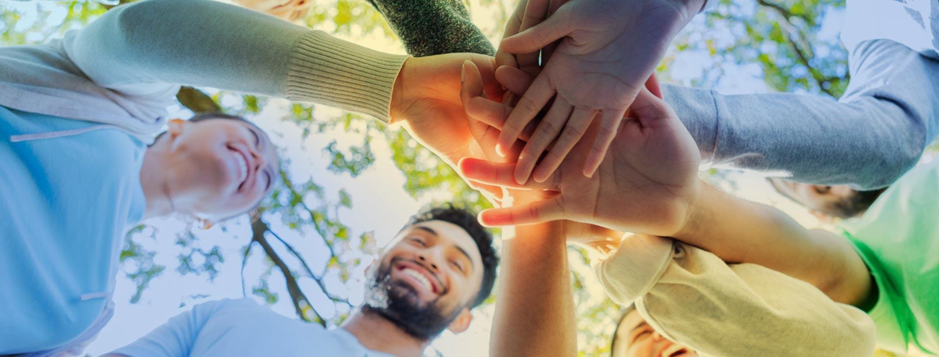 Students stand in circle with hands in the center.