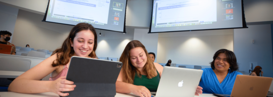 Three students use devices during a hybrid classroom setting