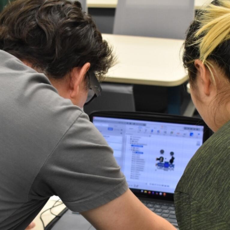 Image of Innovative Media Librarian Alvaro Alvarez (left) and a robotics camps student looking at the computer