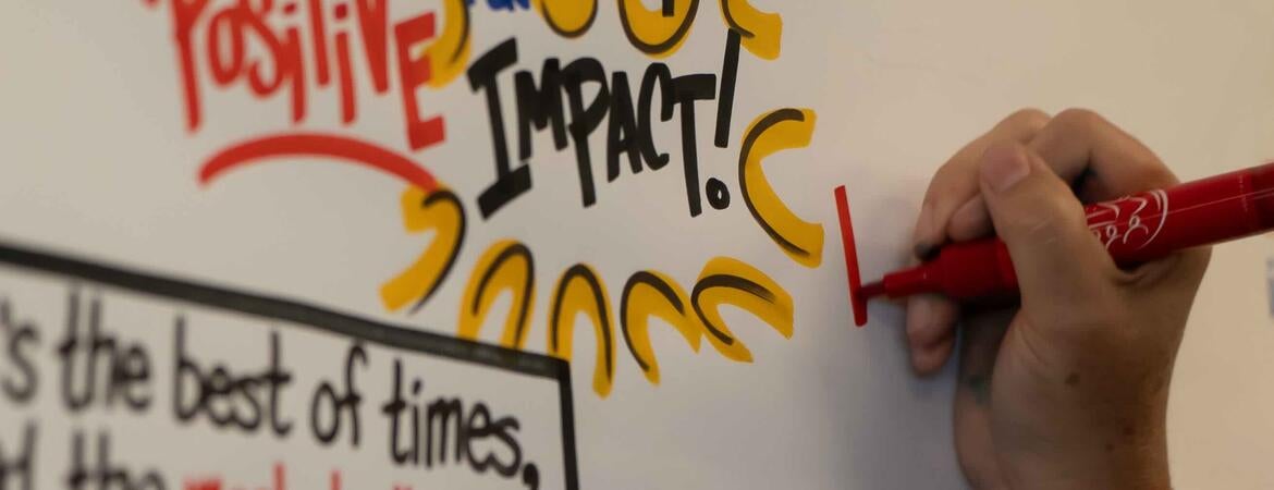 Hand holding a red marker over a board reading "positive impact!"