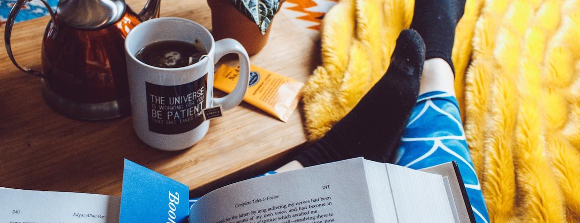 A person reading a book next to a cup of tea