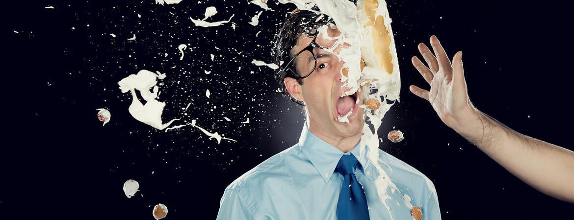 A thrown pie hitting a man's face, knocking off his glasses 