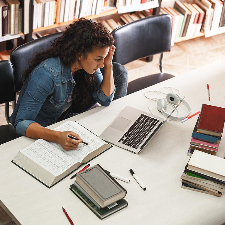 student studying at desk with laptop and textbooks