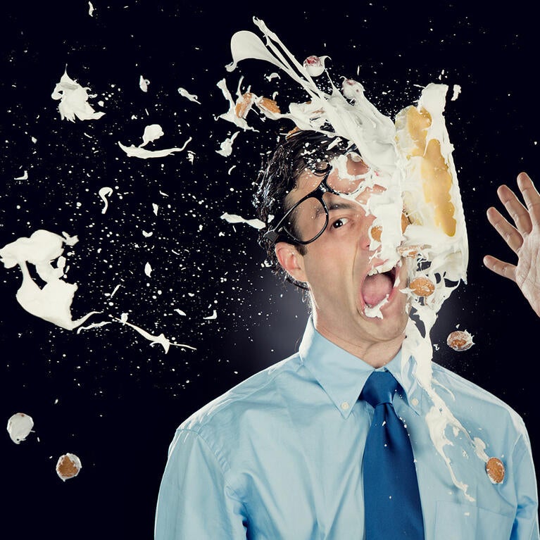 A thrown pie hitting a man's face, knocking off his glasses 