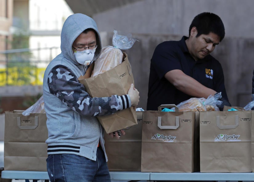 Grad student Jianan Sun walks away with a bag of groceries from R'Pantry staff Humberto Santiago on March 26, 2020 at UC Riverside. Staff with R'Pantry handed out bags of groceries to students after the campus was closed to help prevent the spread of the novel coronavirus. (UCR/Stan Lim)