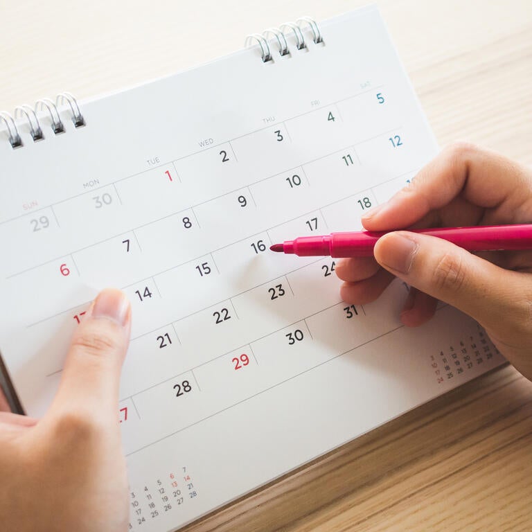A person writing on a calendar with a pen