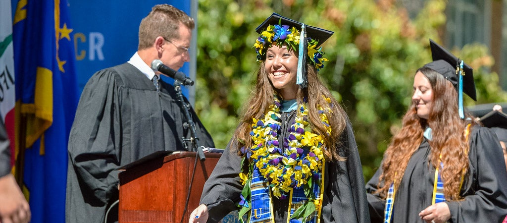 UCR students walk across the stage in their caps and gowns at Commencement. 