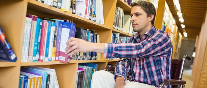A student in a wheelchair browses books on a library shelf. 