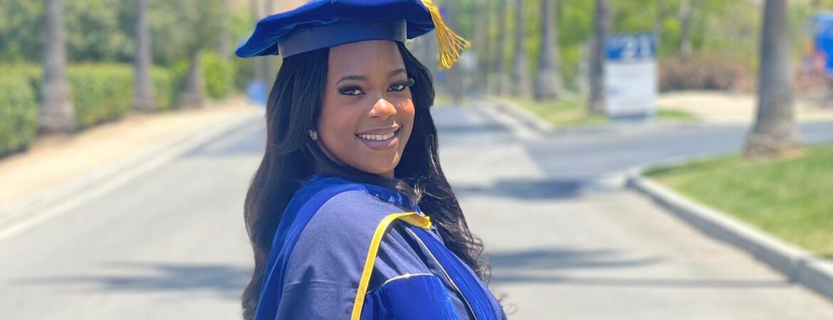 Keziyah Yisrael in graduation regalia on a tree-lined street