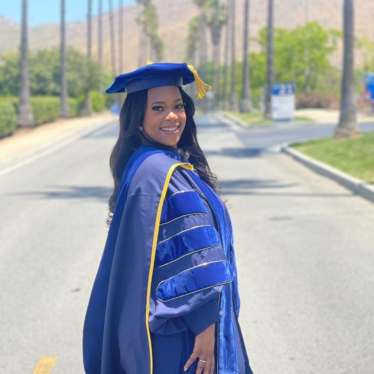 Keziyah Yisrael in graduation regalia on a tree-lined street