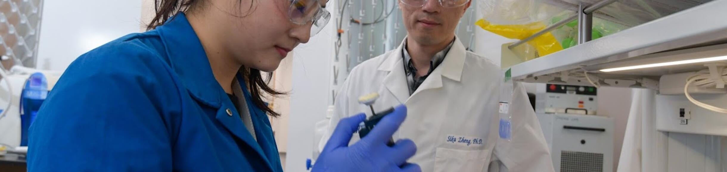 Research assistant supervised by a Researcher prepares a sample for processing.