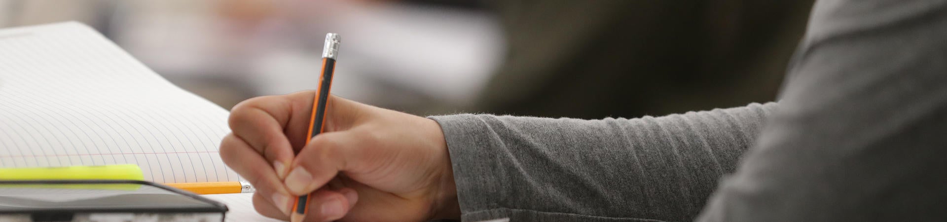This is a closeup image of student holding a pencil, writing in a notebook