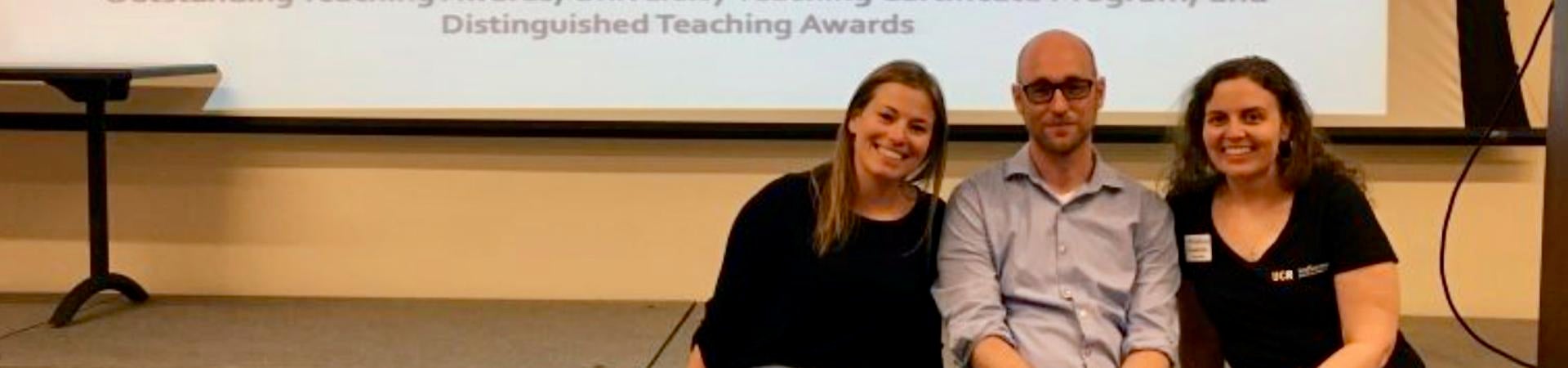 The 2018 TADP team seated on a riser in front of a projected slide celebrating graduate student teaching awards