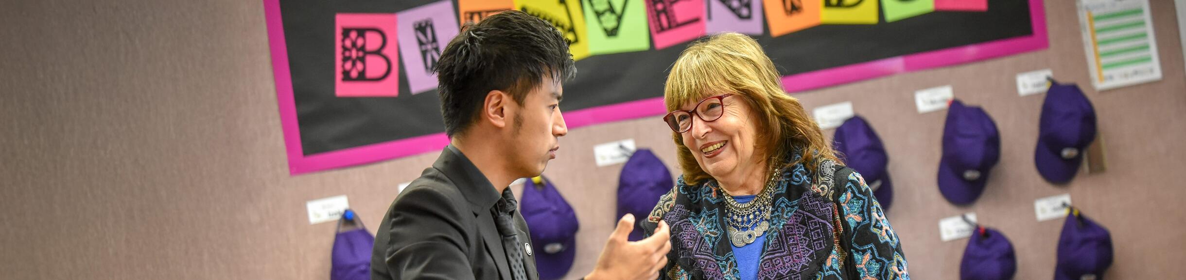 La maestra habla con un invitado en el aula con un cartel de Bienvenidos en el fondo