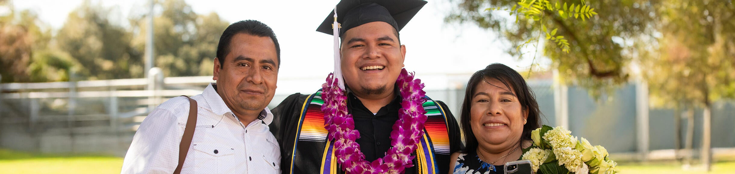 Un graduado es abrazado por sus padres en la ceremonia de graduación de UC Riverside