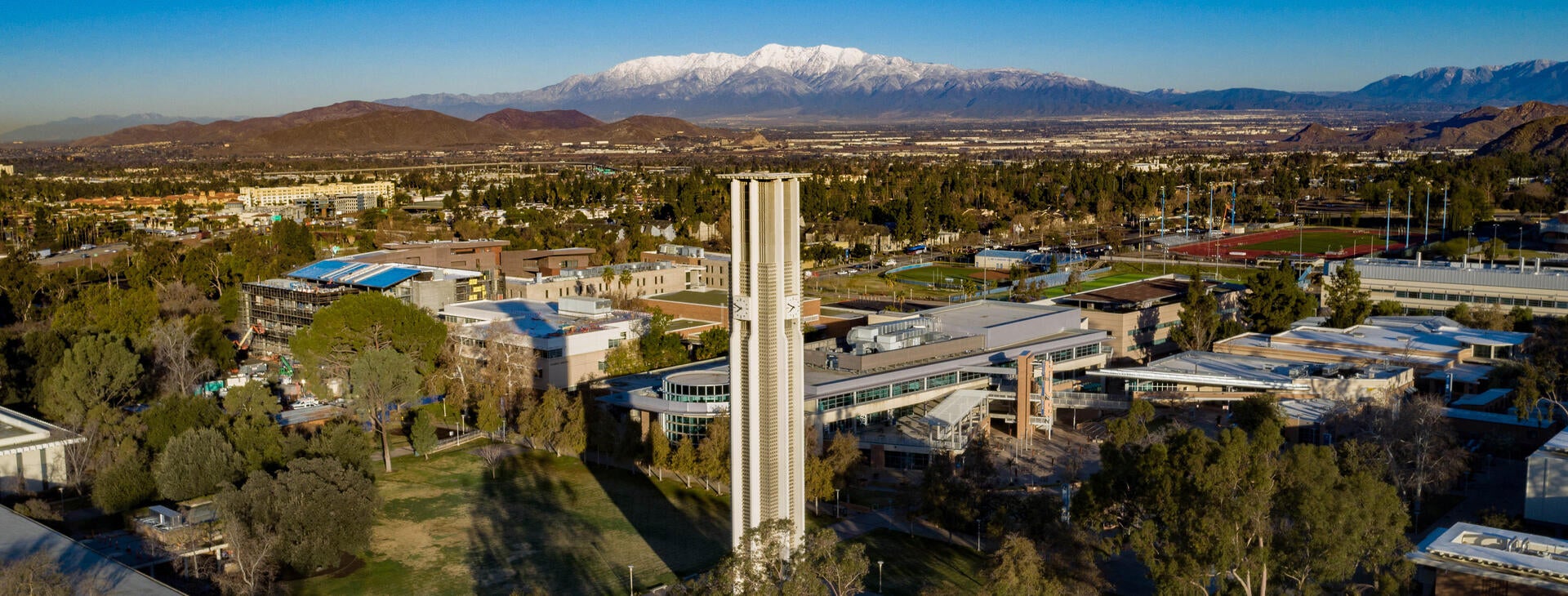 Toma de dron de UC Riverside con la icónica Torre del Campanario en el centro del campus y montañas nevadas en el fondo