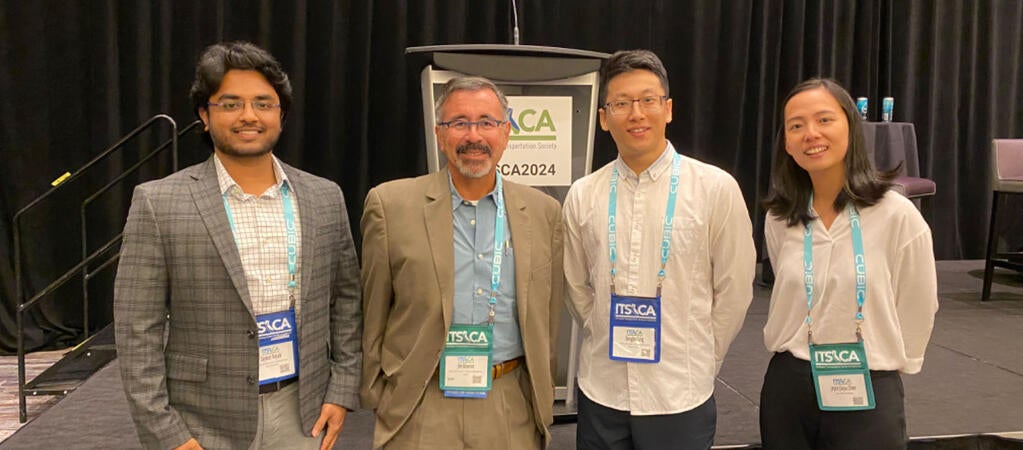 From left to right, Saswat Priyadarshi Nayak, a CE-CERT graduate student, stands next to a attendee, with Dongbo Peng, another CE-CERT graduate student, and a female colleague. All are wearing conference badges and smiling at the camera in front of the ITSCA 2024 podium.