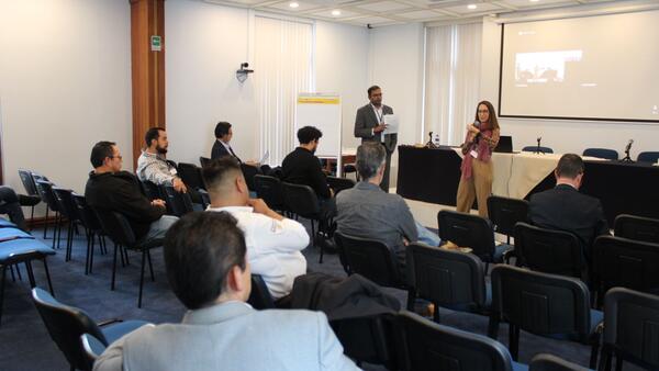 Dr. Arun Raju of CE-CERT and Diana Avalos of AMIVE co-lead a breakout session on infrastructure planning during the Binational Working Group event, speaking to seated attendees in a conference room.