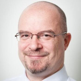 Bald men with glasses and goatee beard wearing white collared shirt smiling at camera with white background