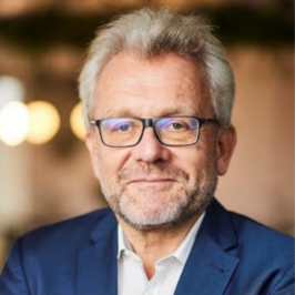 peter schmitting in a blue blazer and whtie collared shirt looking at camera